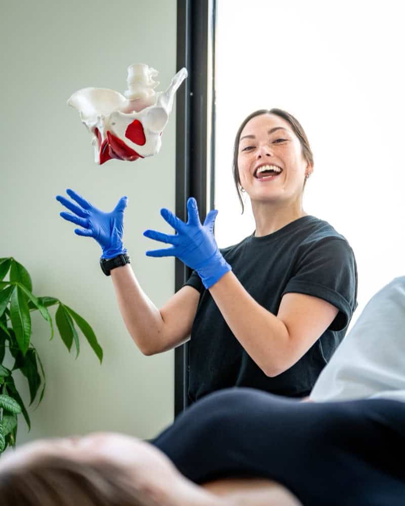 Female physiotherapist demonstrating pelvic anatomy model during consultation.