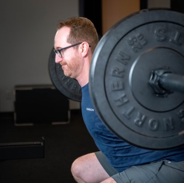 Man performing squat exercise with barbell at South Island Physiotherapy clinic.