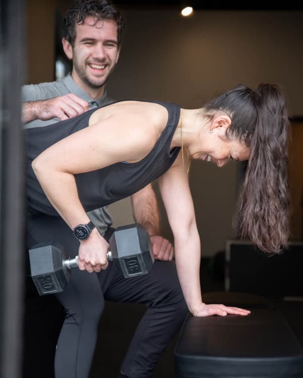 Physiotherapist assisting a woman with weight training exercises using dumbbells.