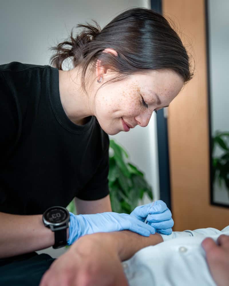 Female physiotherapist in black shirt with blue gloves performing physical therapy on patient.