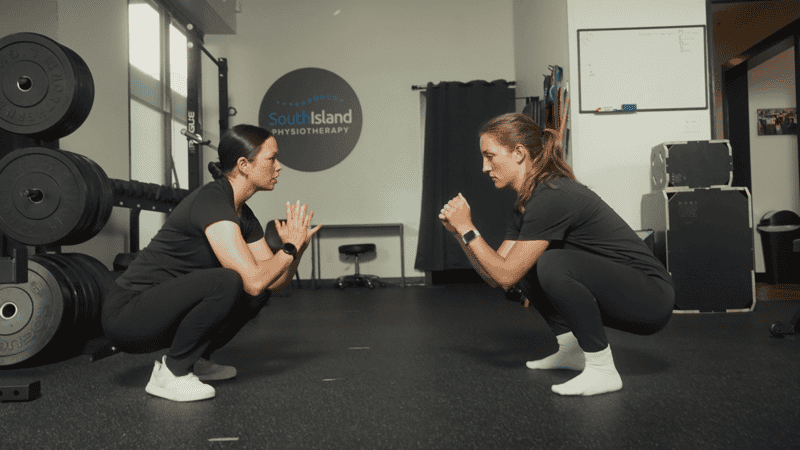 Two women practicing squat exercises in physiotherapy clinic.