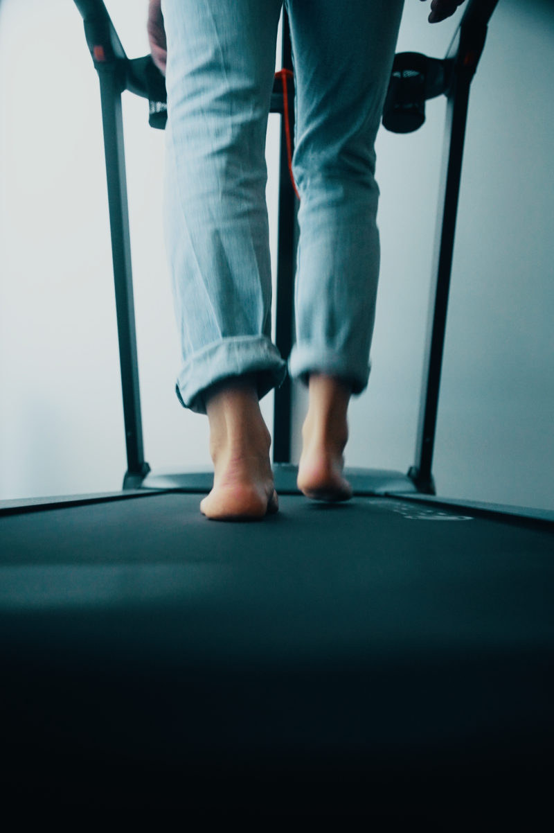 Person walking barefoot on treadmill during physiotherapy session.