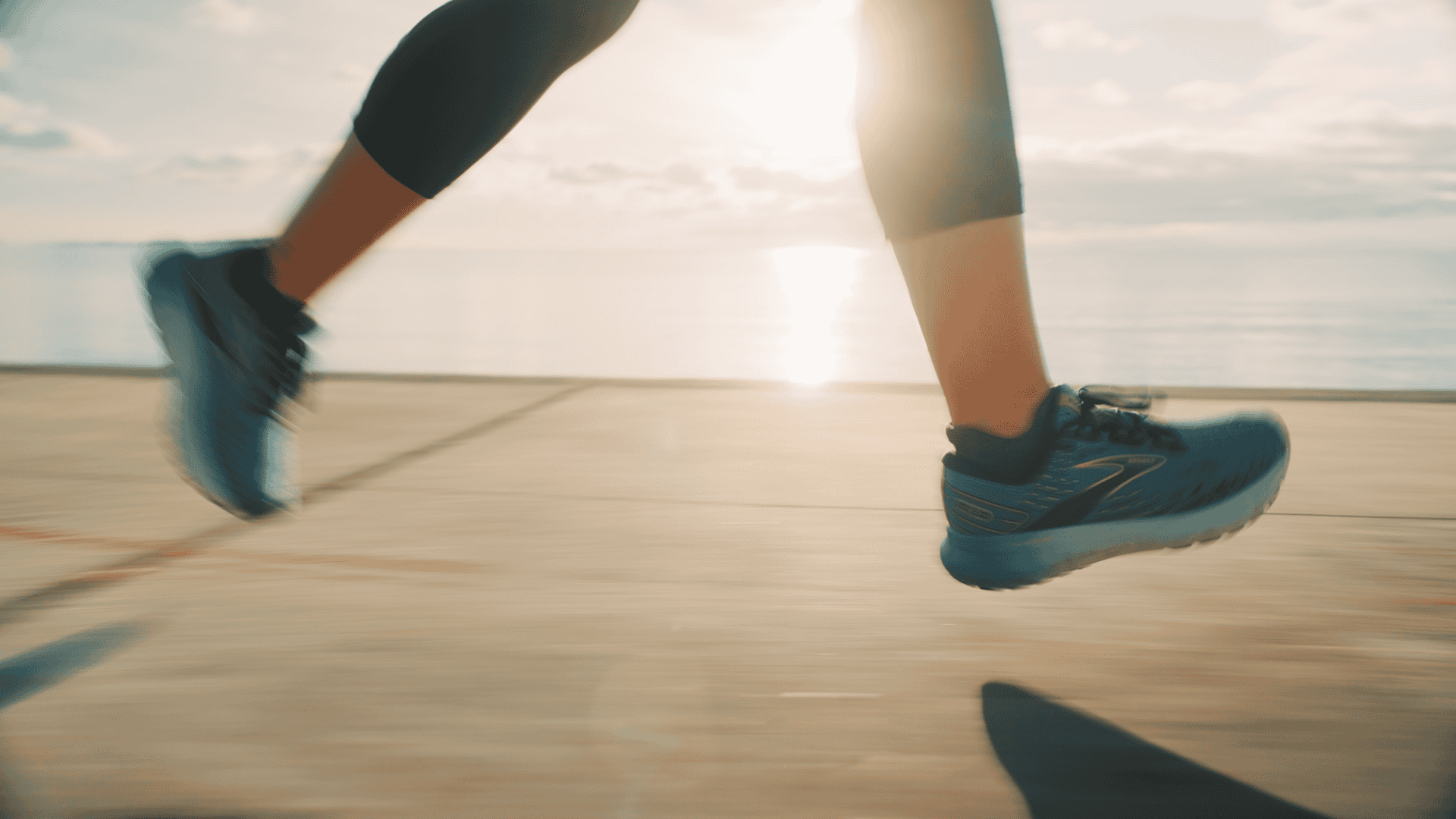 Person running outdoors in athletic shoes on a wooden path.