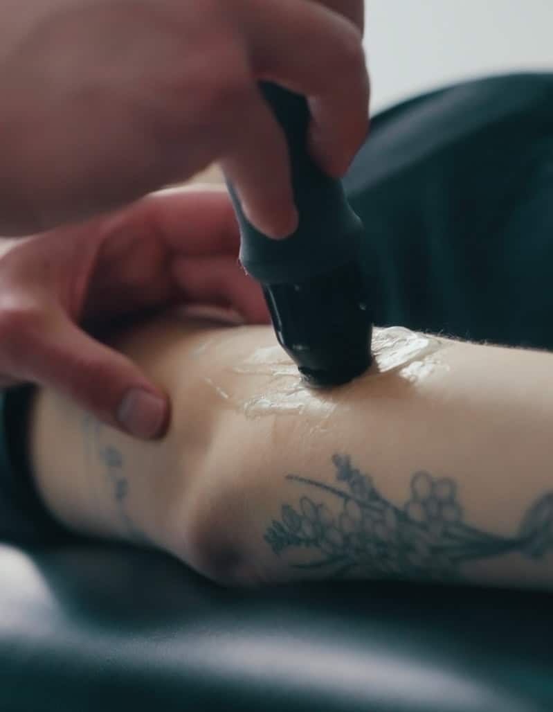 Physiotherapist applying ultrasound therapy to patient's arm for pain relief and healing.